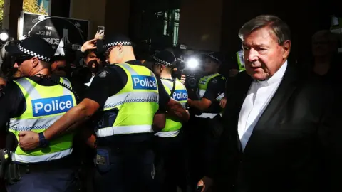 Getty Images A line of police hold back media and spectators to allow George Pell to leave the Melbourne Magistrate's Court in May