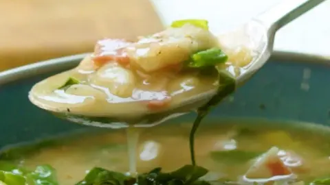 Close-up of the white bean and bacon soup on a spoon over a green bowl.