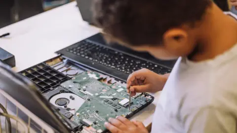 A boy repairing a laptop with a small screwdriver.