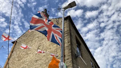 A Union Flag and Irish Tricolour tied to a lamppost and drainpipe next to a terraced house (taken Thurs, 25 June)