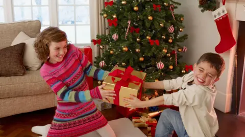 Getty Images Boy and girl tugging at a Christmas gift in living room