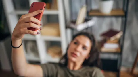As imagens de garagem são mostradas uma mulher em uma camiseta verde na cadeira, a mão está na cabeça quando segura o telefone para pegar a selfie.