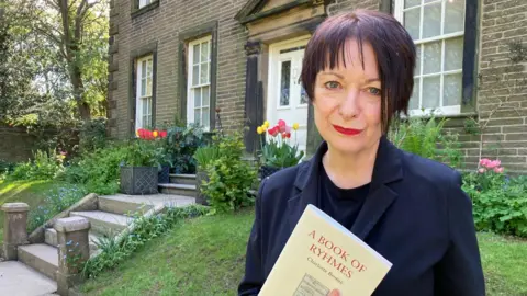 A woman holding a book standing outside the Brontë Parsonage Museum.