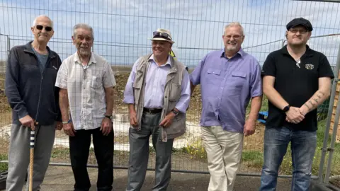 BBC The group who are behind the memorial standing in front of the fenced-off site