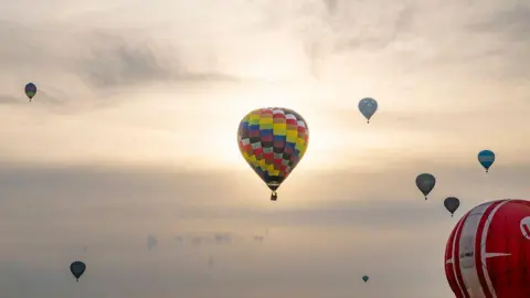 Claire Hartley A number of hot-air balloons in the early-morning sky.