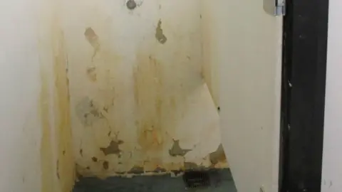 HM Chief Inspector of Prisons A old shower with paint and plaster coming off the walls and yellow grime everywhere