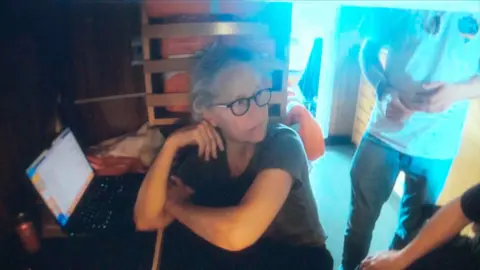 Wendy Rush, a woman in a grey t-shirt, looks away from a laptop with an anxious expression