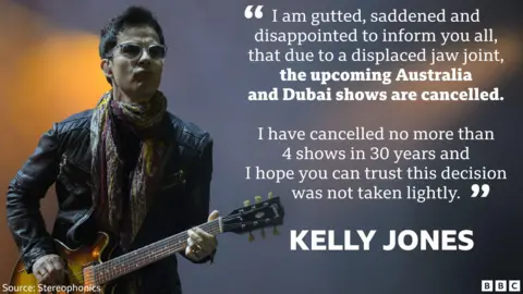 Stereophonics' Kelly Jones on stage, playing guitar. He is wearing a black leather jacket and a pair of glasses.