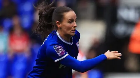 Getty Images Maria Boswell of Ipswich Town Women is seen in action during a match. She is wearing a blue top and has her long hair tied back.