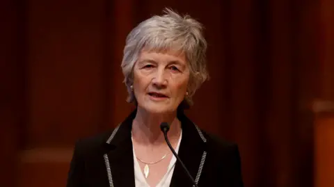 Catherine Connolly speaking into a microphone. She is wearing a white top and a black suit jacket. 
