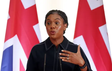 Kemi Badenoch giving a speech in front of two Union Jacks.
