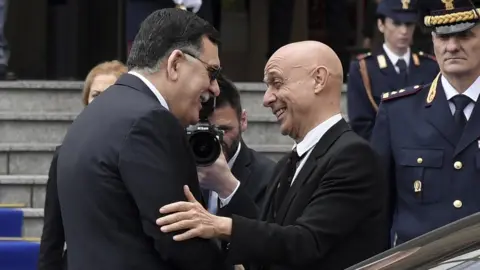 Getty Images Marco Minniti (R) greets Libya's Prime Minister Fayez al-Sarraj