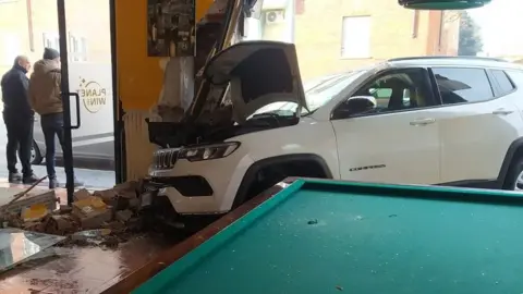 Car inside cafe after crash with smashed window and bricks on floor