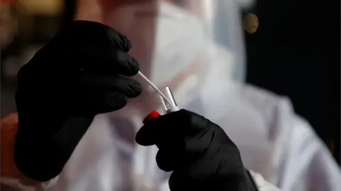 Reuters A health worker, wearing a protective suit and a face mask, holds a test tube after administering a nasal swab to a patient in a temporary testing site for the coronavirus disease (COVID-19) at the Zenith Arena in Lille, France, October 15, 2020.