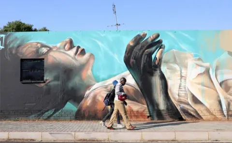 EPA A couple walk past an art work by German artist @norm_abartig and South African artist @dekor as part of the Westdene Graffiti Project in downtown Johannesburg, South Africa, 09 October 2018.