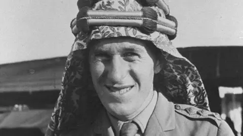 A black and white head and shoulders picture of a man who has military uniform on and an Arabic head scarf.