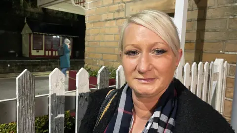 Woman with short blonde hair and a tartan scarf at a railway station