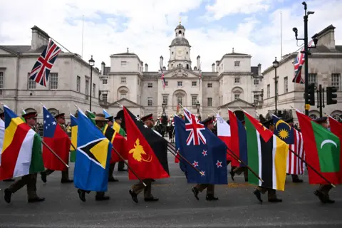 PA Media Members of the procession carry flags of the Commonwealth nations while wearing uniforms and hats, in front of a building in central London.