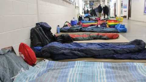 Light Project Peterborough Sleeping bags laid out on the floor of a concourse in the stadium. People are gathered in the distance.