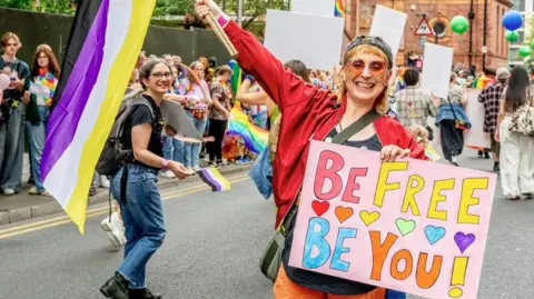 A woman is holding a colourful sign which reads: "Be Free Be You" as part of the Manchester Pride 2025 parade. 