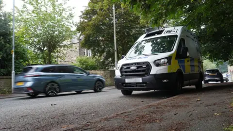 A blurred blue car speeds past a police speed camera van on a residential street.