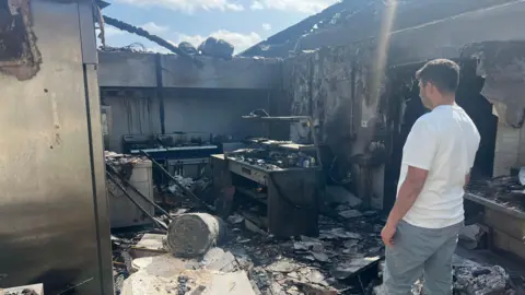 Mr Acharya in white tshirt and blue jeans looking at badly burned building