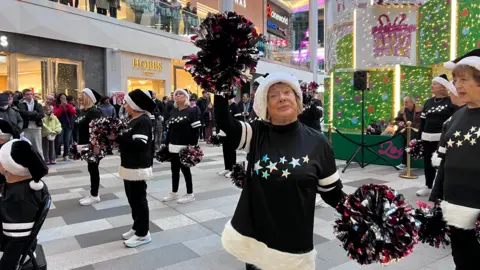 Lily-May Symonds/BBC One performer in the foreground has an arm raised with a pom-pom, while others stand in formation behind. 