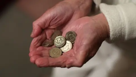 A stock image showing a close-up of an elderly person's hands holding pound coins in their cupped hands.