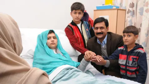 Getty Images Malala sits up in her hospital bed with her father Ziauddin and her two younger brothers, Atal on the right and Khushal in the centre.