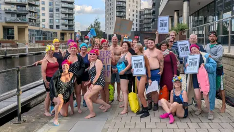 A group of people in swimming costumes pose for a photo. Some of them are holding banners which read 'Right to Swim'.