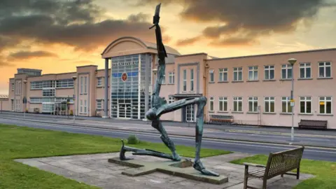 A three legs of man outside the airport terminal buildings at dusk.
