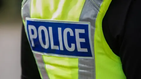 The back view of a British police officers yellow vest with the word 'POLICE' in bold white lettering.