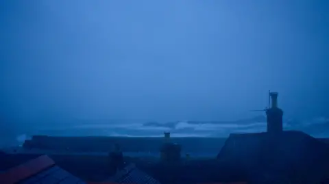 BBC Weather Watchers/Mousehole Pat Strong waves seen off the coastline in Cornwall with houses in the foreground