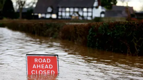 Reuters/Carl Recine A sign partially submerged in Severn Stoke, from flooding after heavy rain from Storm Henk in 2024. 