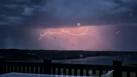 Johnnieb A lightning bolt coming from a large dark cloud. It has made the sky look bright pink. 