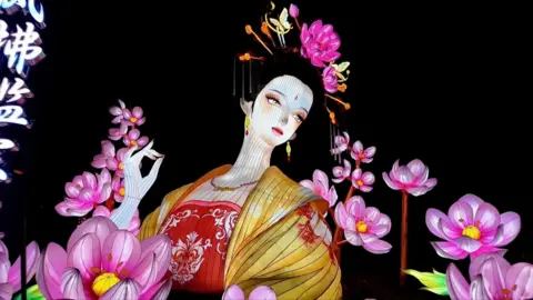 Lantern figurine of woman in traditional Chinese dress surrounded by pink flowers
