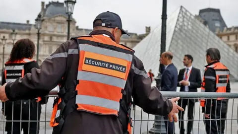 Security employees install barriers near the glass Pyramid of the Louvre Museum in Paris, France