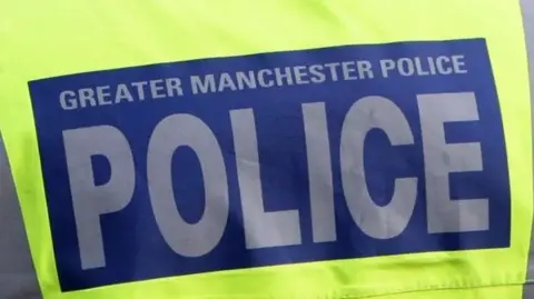 Close-up image of a police vest. Luminous yellow in colour with a blue box in the middle - within which 'Greater Manchester Police' is written in grey text