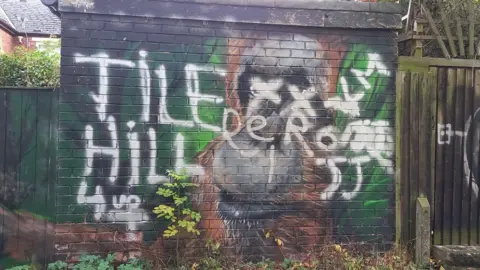 Martin Prue A mural of an orangutans painted on a wall in front of houses that has been vandalised with white graffiti. 