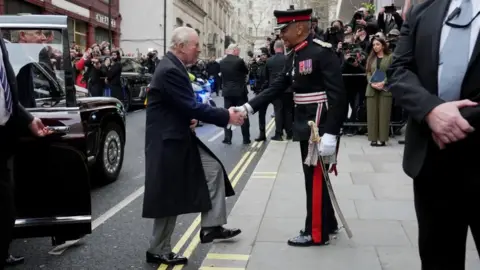 King Charles shaking hands with a man in army attire as he leaves a car in centra London