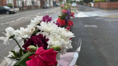 A close-up view of a bunch of flowers tied to some railings. The flowers are white, pink and burgundy.