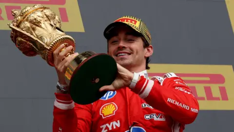Ferrari's Charles Leclerc smiles while holding the British Grand Prix winner's trophy