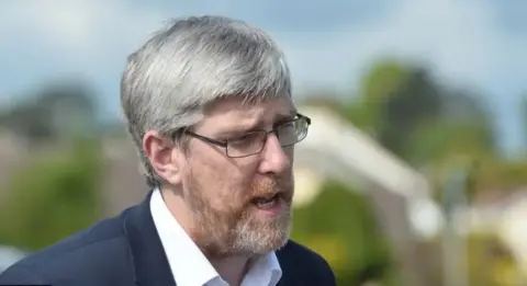 Pacemaker John O'Dowd in a suit, wearing his glasses and standing outside 