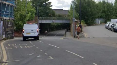 Google A white van travels past a bus stop on a main road, with a slip road branching off to the right.