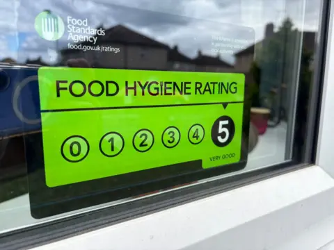 A green sign with the words "food hygiene rating" displayed on the inside of a window