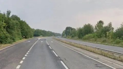 Google A stock shot of the A5 showing four lanes - two in each direction - with a slip road on the left of the shot. The road is empty, apart from one car in the distance approaching the camera.