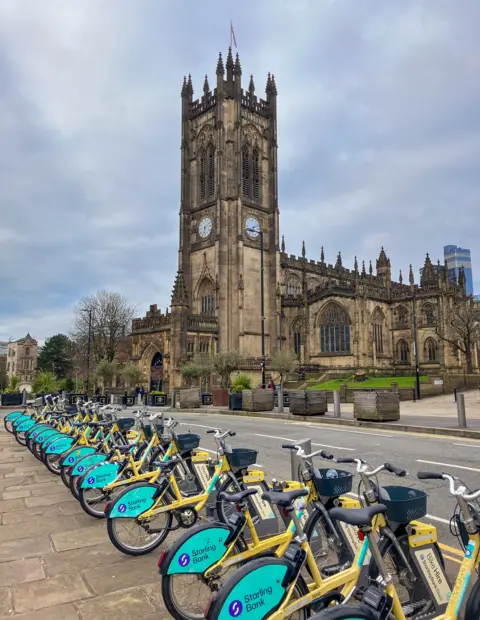 Rows of Starling Bank Bikes at a docking station in front of Manchester cathedral.