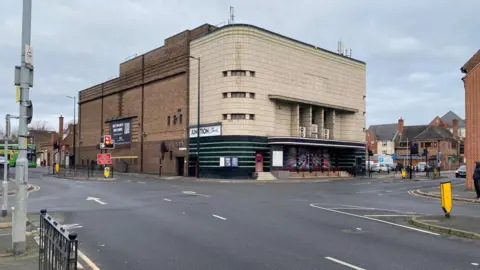 The outside of Beacon Bingo in Baxter Gate. The front of the building is made up of a grey terracotta tile material. A crossroad can be seen in front of the shot. 