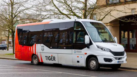 Side-on view of a red and white Tiger bus