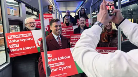 A smiling Ken Skates and Labour activists on a bus holding placards saying vote Welsh Labour.